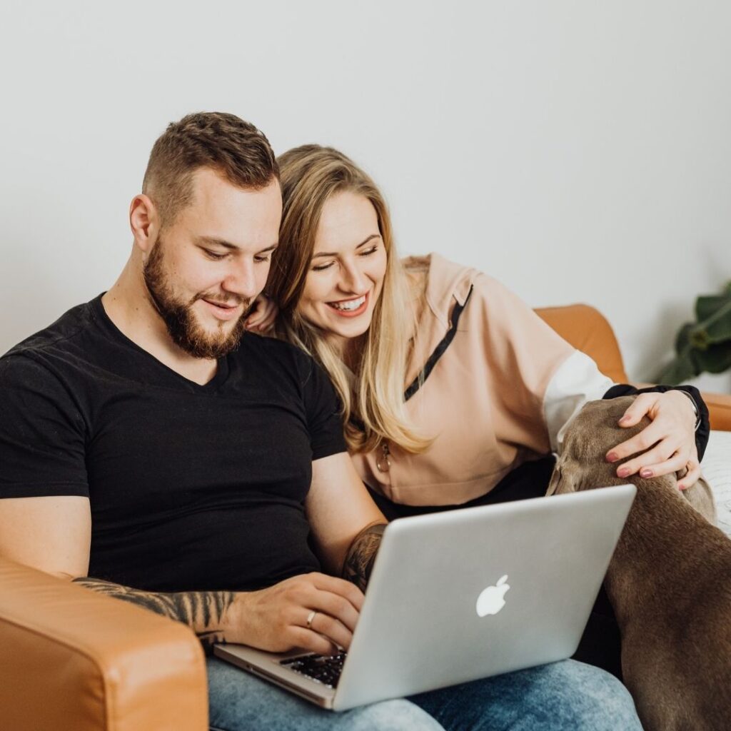 couple with dog looking at houses on laptop